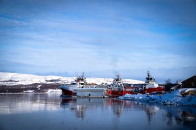 Rödvita ryska fartyg ligger vid en hamn. Snötäckta berg i bakgrunden.