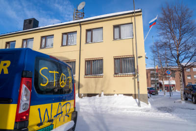 En bil i Ukrainas flaggas färger med texten Stop War. I bakgrunden syns ett hus med Rysslands flagga.