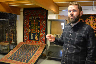 John Björkman, en person med mörkt helskägg och gråsvart rutig skjorta, förevisar ryor på en utställning på museet..