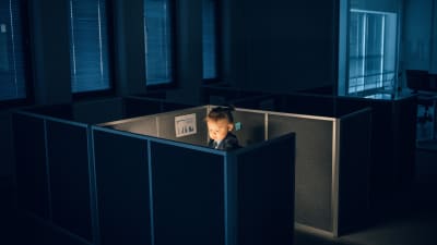 Barn sitter i mörkt kontorslandskap