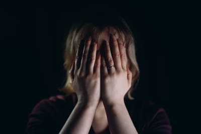 En person med vigselring på vänster hand håller händerna för sitt ansikte.