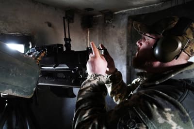 En man i en bunker med hörselskydd på som siktar med ett vapen.