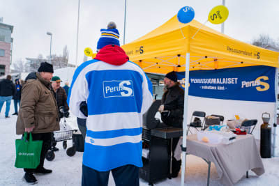 Valkampanj bid Sannfinländarnas valtält. I förgrunden syns en person som har Sannfinländarnas logo på ryggen.