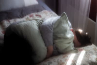 En person liger i fosterställning i en säng och kramar om en stor dyna.