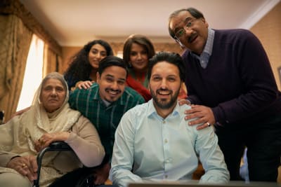 En stor och glad indisk familj tittar skrattande in i kameran.