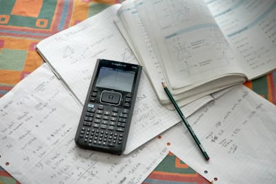 En miniräknare, papper och en matematikbok på ett bord.