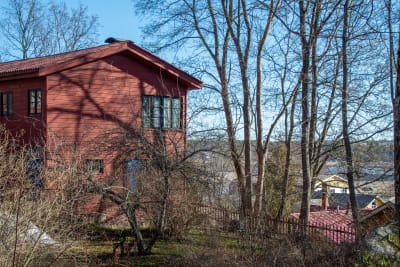 Rött trähus på en gård på en kulle med utsikt över ett trähusområde. 