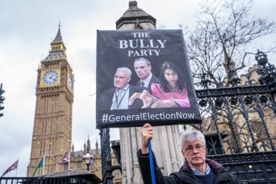 En demonstrant håller upp ett plakat med bilder av brittiska politiker som anklagas för mobbning.