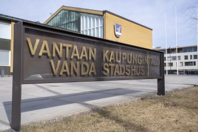 Enskylt med texten Vanda stadshus. i Bakgrunden syns stadshuset med kommunvapnet på väggen.
