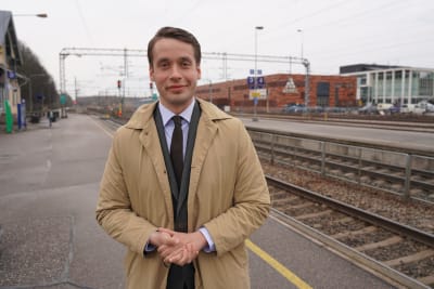 En man i kostym och jacka står vid en perrong på en tågstation. Han heter Henrik Wickström.