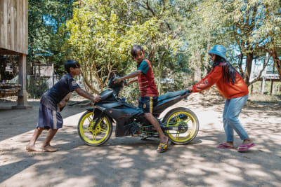 Lean Tat (oik.) ja nuorempi veli (kesk.) ja naapurin poika siirtävät moottoripyörää kotonaan Mekong joen varressa Stung Trengin alueella Pohjois-Kambodžassa.
