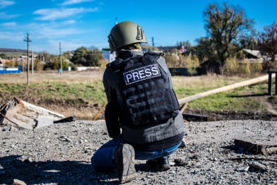 En fotograf iklädd skyddshjälm och skyddsväst där det står "press" på ryggen hukar för att ta en bild i Bachmut.