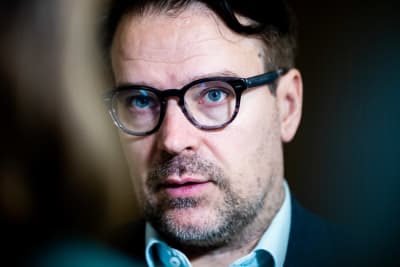 En man med svartbågade glasögon i närbild.
