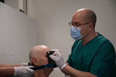 En person i vårdarkläder placerar en ram på en patients huvud. 
