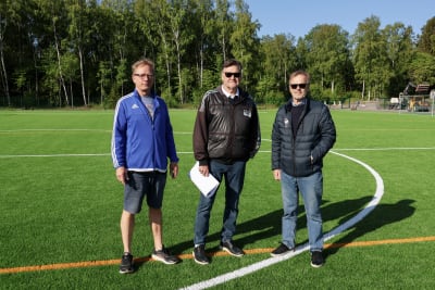 Tre medelålders män står på en fotbollsplan.