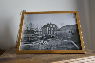 Svartvitt fotografi av en gammal herrgård i två våningar med kringliggande byggnader