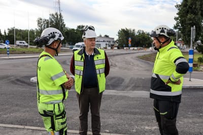 Tre män med byggarbetshjälm och reflexvästar står framför en rondell.