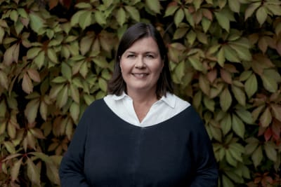 Aija Kaski fotograferad vid en vägg med växtlighet.
