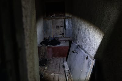 Ett mörkt utrymme som är mycket smutsigt och dammigt. I utrymmet ligger en dörr på golvet och en militäruniform.