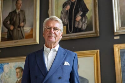 Björn Wahlroos poserar framför Yles vägg med porträtt av före detta chefer.