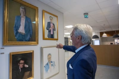 Björn Wahlroos pekar mot en vägg fylld av porträtt av före detta Ylechefer. 