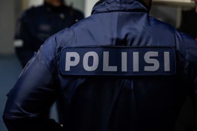 På bilden syns en person i polisdräkt. Personen står med ryggen till med texten "poliisi" på ryggen.