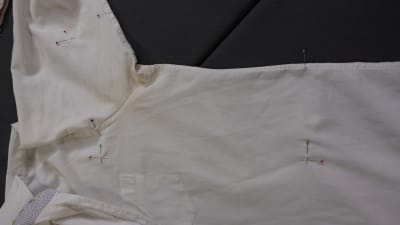 En närbild av en vit skjorta där ärmen och sidan syns. Flera knappnålar är placerade på skjortan.
