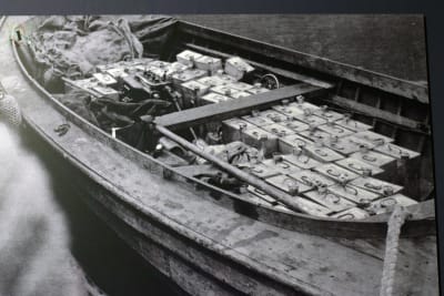 En svartvit bild av en båt fylld med dunkar med smuggelsprit.