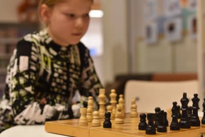 En ung flicka med ljust hår i svans spelar schack.