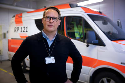 Porträttfoto av man i glasögon framför vit och röd ambulansbil
