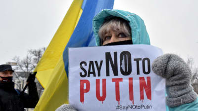 En kvinna håller i en skylt med texten "Say no to Putin". Ukrainas flagga syns i bakgrunden.