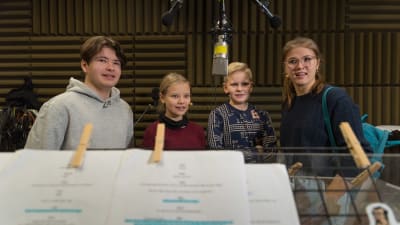 Fyra ungdomar står i en studio och skådespelar i ett audiodrama. De ser mot regissören som står bakom kameran.