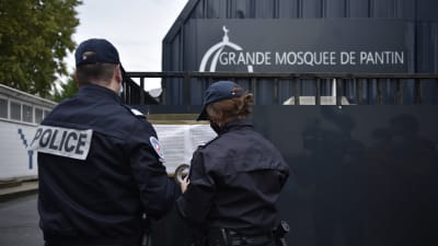 Bild på moské och två poliser som står utanför och läser en lapp med ryggarna mot kameran.