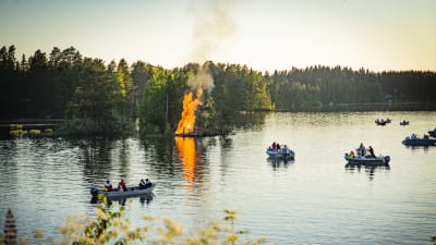 Juhannuskokko Haukivuoren Kapustasalmessa. Sää 2022 oli lämmin ja paikalla on kymmeniä veneitä. Kokko palaa pienessä saaressa.