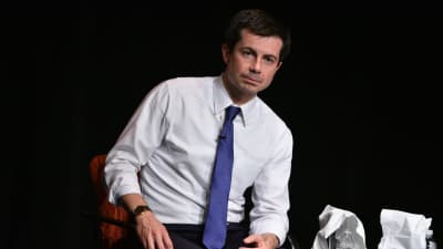 En man i vit skjorta med blå slips sitter på en stol framför kameran. 