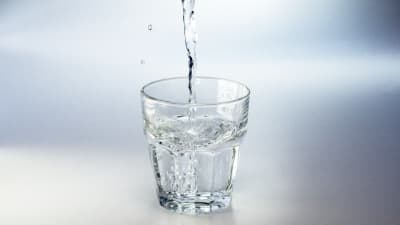 Vatten som rinner i ett glas mot en neutral vit bakgrund.
