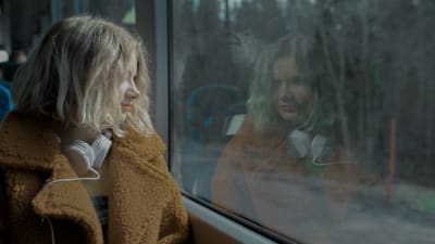 En ung flicka sitter och tittar ut genom ett bussfönster.