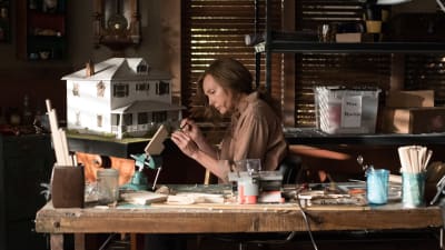 Annie (Toni Colette) sitter och gör miniatyrer vid ett bord. 