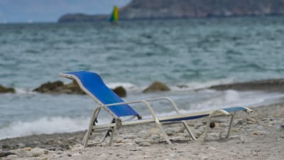En tom solstol vid en blåsig strand.