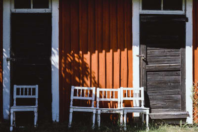 Valkoisia tuoleja, taustalla punainen puutalon seinä