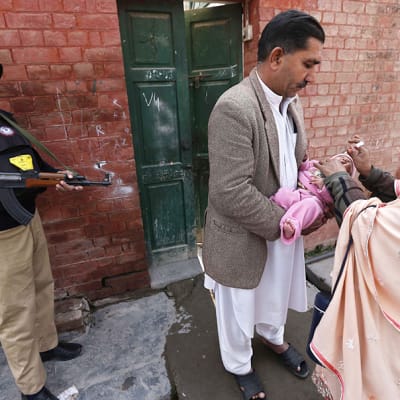 Vartija turvasi terveydenhoitajien työta Peshawarissa, Pakistanissa, kun he rokottivat lapsia poliota vastaan helmikuussa 2014. Useita rokottajia on surmattu Pakistanissa, sillä heitä on epäilty Yhdysvaltain vakoojiksi.