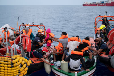 Migranter räddas på Medelhavet. Flera män lyfter över barn till gummibåt.