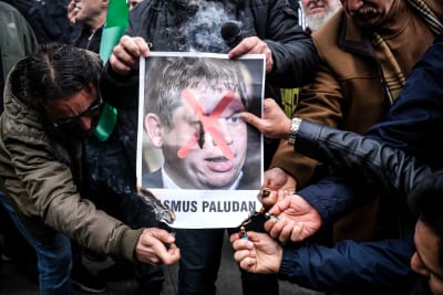 Människor håller upp en bild av Rasmus Paludan med ett rött kors över.