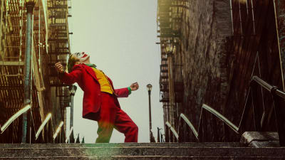 Joker (Joaquin Phoenix) iklädd clownmask och röd kostym står uppe på en trappa och dansar.