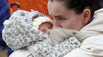 En kvinna pussar en liten bebis på kinden. Hon håller i bebisen.