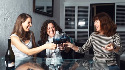 Tre skrattande kvinnor skålar i rödvin