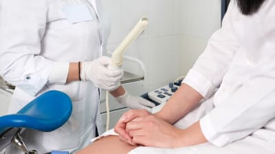 En gynekolog håller i en ultraljusstav. En kvinna sitter i gynekologstol bredvid.