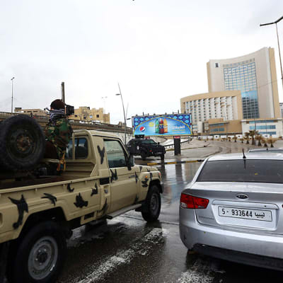 Libyan turvallisuusjoukkojen edustajia Tripolin Corinthia-hotellin ulkopuolella 27. tammikuuta. Edessä on Toyotan pickup-auto, jonka lavalla on mies aselaitteensa kanssa.