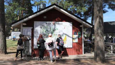 En skylt med texten "Nagu" och "Nauvo. Några kvinnor läser skylten.