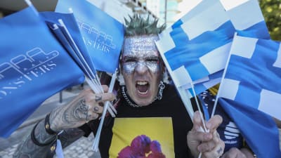 En man med många Finlandsflaggor och Saara Aalto-flaggor visar tänderna.